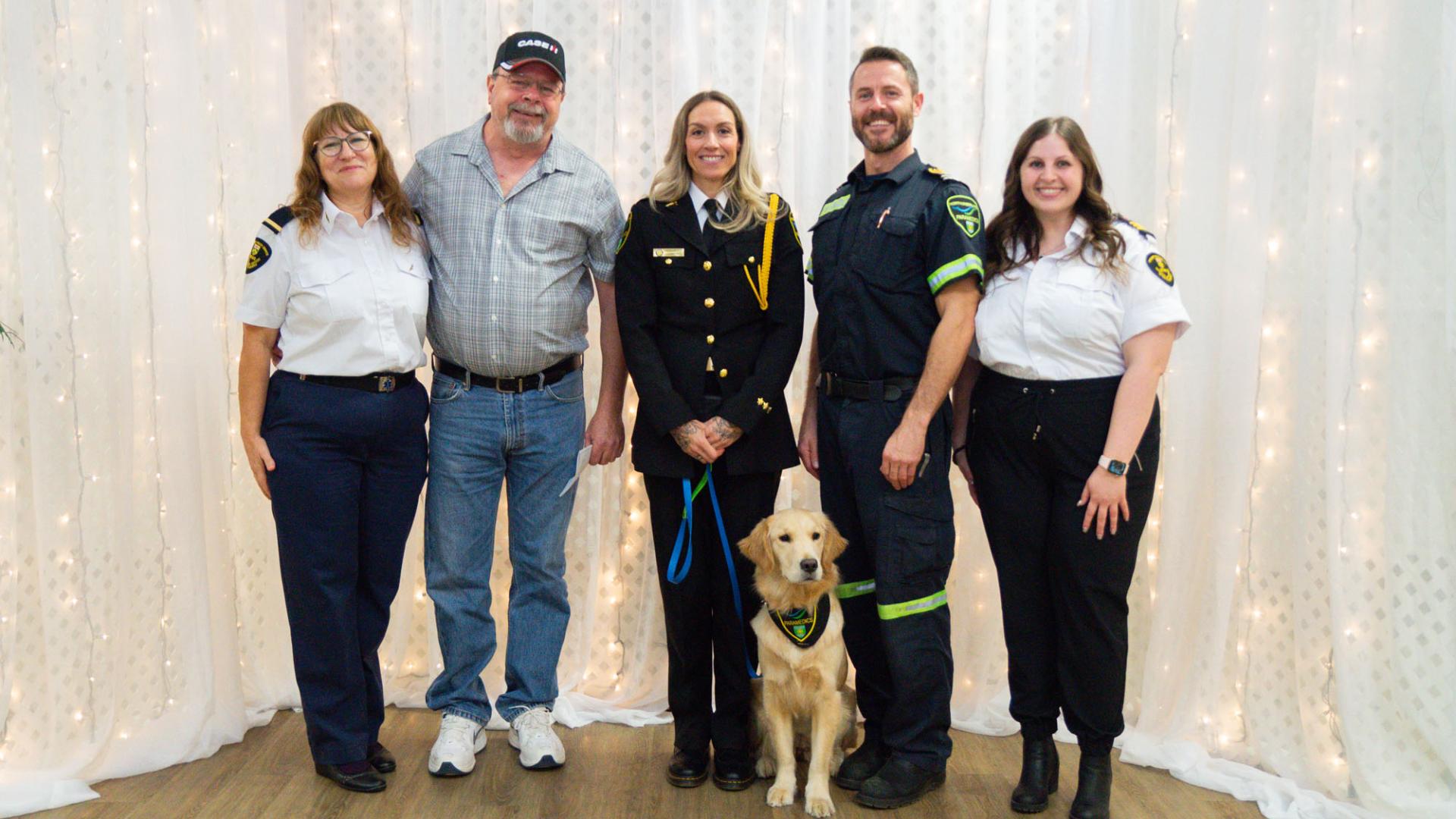 White man in casual clothing lined up beside four white officers and a golden lab dog
