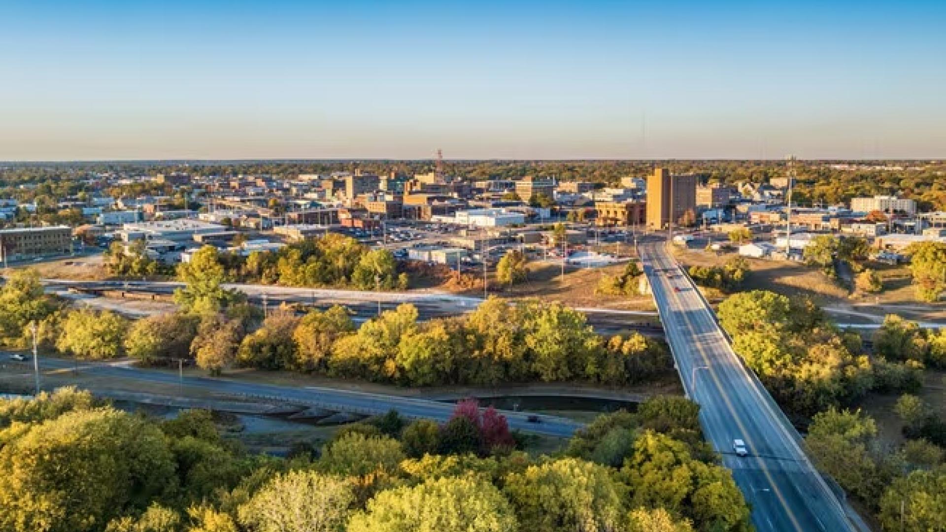 Cityscape with trees, roads, and buildings under a clear blue sky.