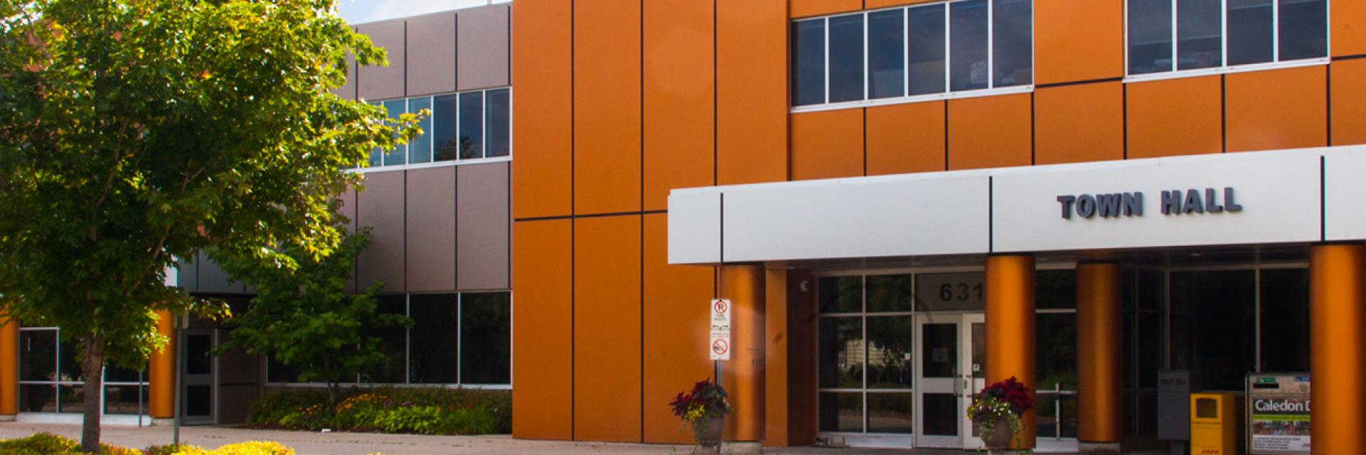 Modern orange building with "Town Hall" sign, large windows, and a tree in front.
