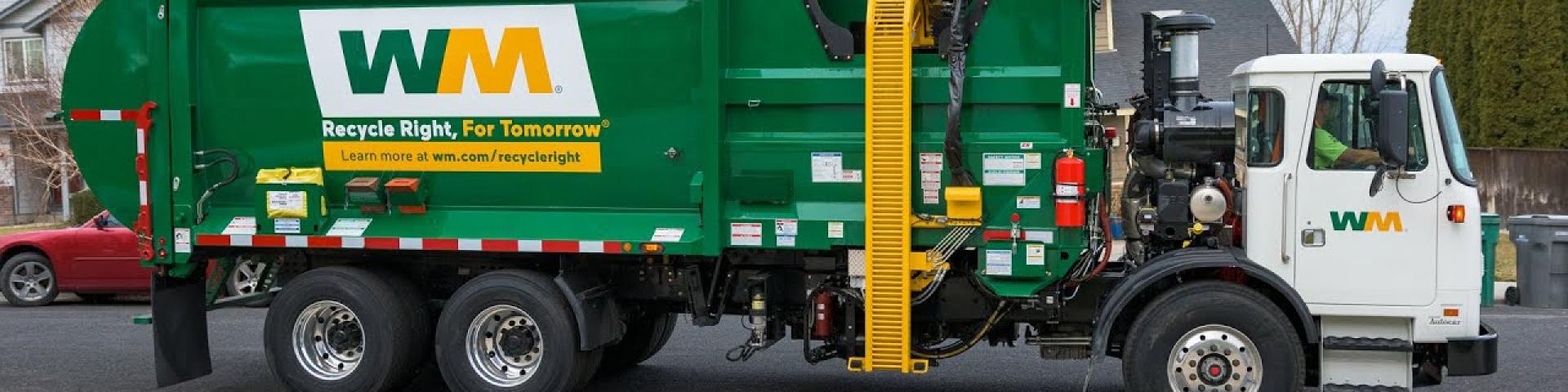 Green and white WM garbage truck parked on a suburban street.